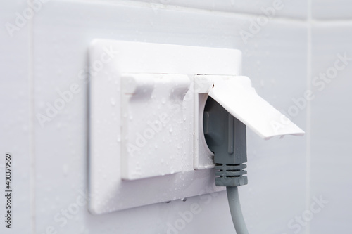 Weatherproof socket on a white tiled wall with water droplets.