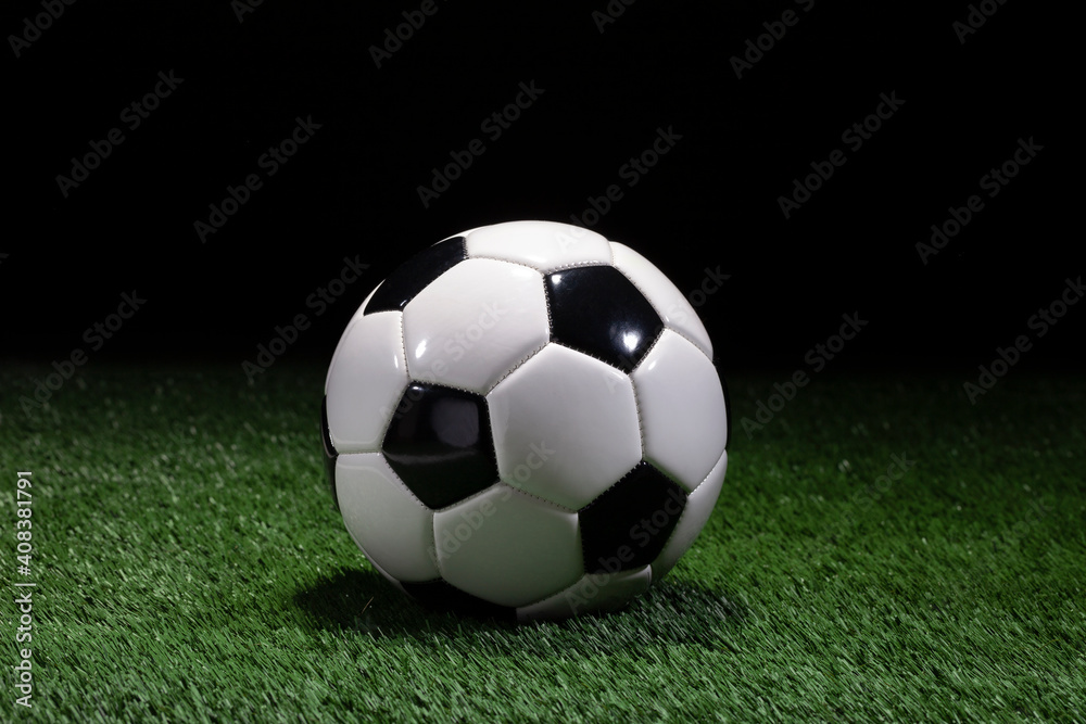 Traditional black and white soccer ball on green field with dark background