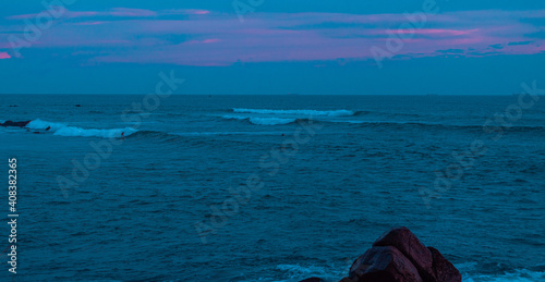 Krajobraz fal na oceanie podczas zachodu słońca przy skalistym wybrzeżu.