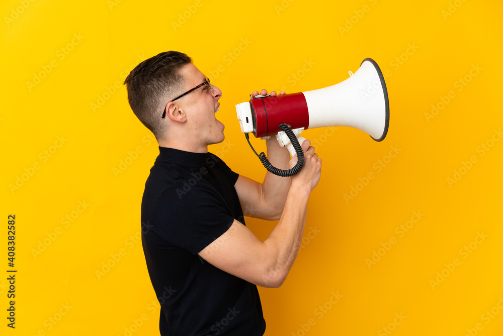 Young caucasian man isolated on yellow background shouting through a megaphone to announce something in lateral position Young caucasian man isolated on yellow background shouting through a megaphone to announce something in lateral position