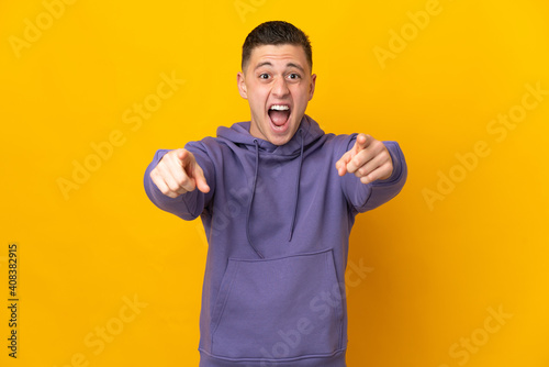 Young caucasian man isolated on yellow background surprised and pointing front
