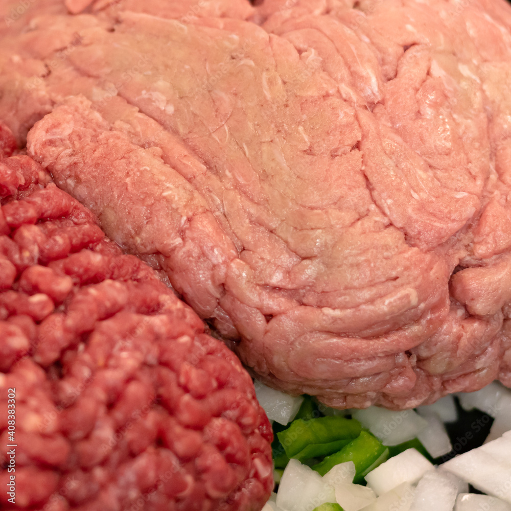 Raw ground meats sitting on a bed of raw onions and green bell peppers in non-stick skillet on a stove top in a domestic kitchen. Raw ground meats sitting on a bed of raw onions and green bell peppers in non-stick skillet on a stove top in a domestic kitchen.