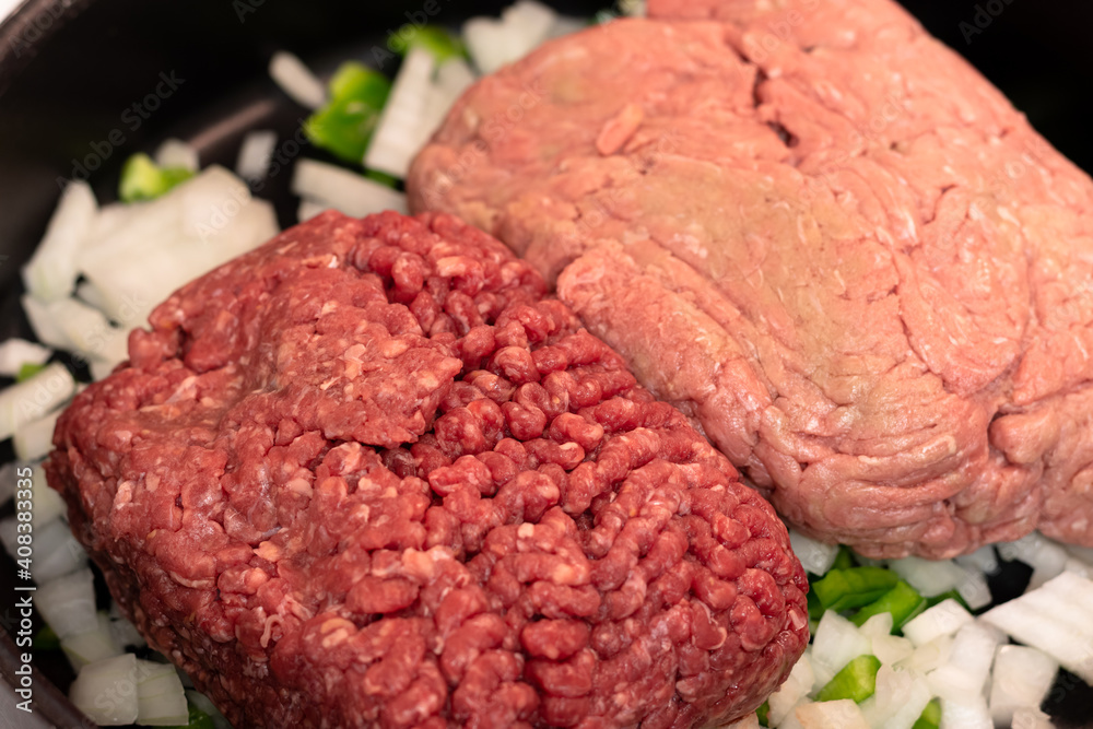 Raw ground meats sitting on a bed of raw onions and green bell peppers in non-stick skillet on a stove top in a domestic kitchen. Raw ground meats sitting on a bed of raw onions and green bell peppers in non-stick skillet on a stove top in a domestic kitchen.