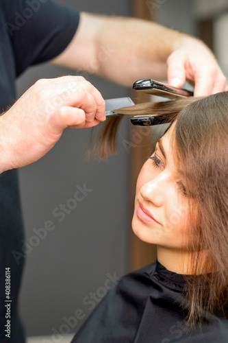 A male hairdresser is straightening the hair of the young woman in a beauty salon