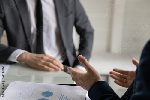 Close up two business partners discussing project statistics at meeting, sitting at table in office, businessmen colleagues wearing suits brainstorming, working on financial report together
