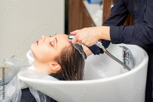 A female hairdresser is rinsing the hair of a young woman in a sink after shampooing in a hair salon