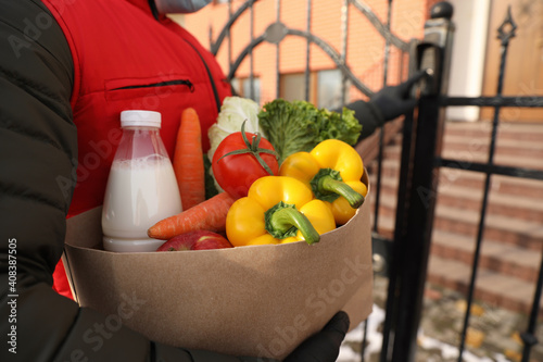 Fototapeta Naklejka Na Ścianę i Meble -  Closeup view of courier ringing gate bell outdoors, focus on paper bag with groceries. Delivery service during quarantine due to Covid-19 outbreak