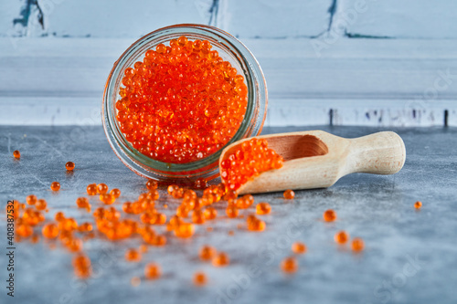 A jar of red caviar and wooden spoon on marble background