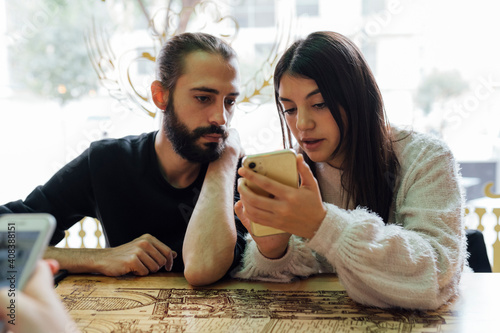 Young friends using smart phone while sitting in restaurant