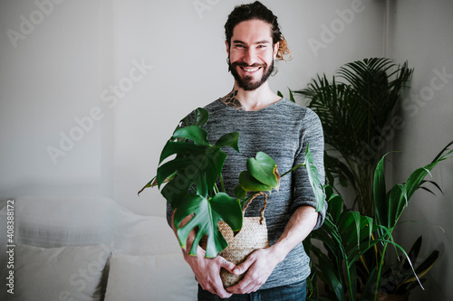 Young man smiling while holding Monstera plant at home