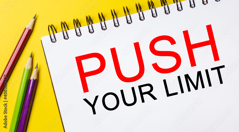 PUSH YOUR LIMIT on a white notepad with pencils on a yellow background. Business concept PUSH YOUR LIMIT on a white notepad with pencils on a yellow background. Business concept