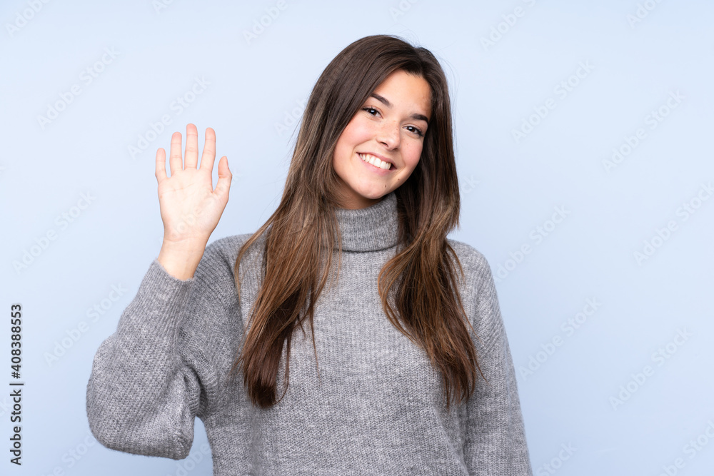 Teenager Brazilian girl over isolated blue background saluting with hand with happy expression