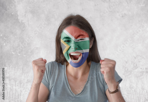 Young woman with painted flag of South Africa and open mouth looking energetic with fists up