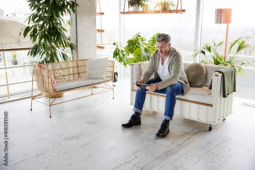 Mature man using digital tablet while sitting on sofa at home