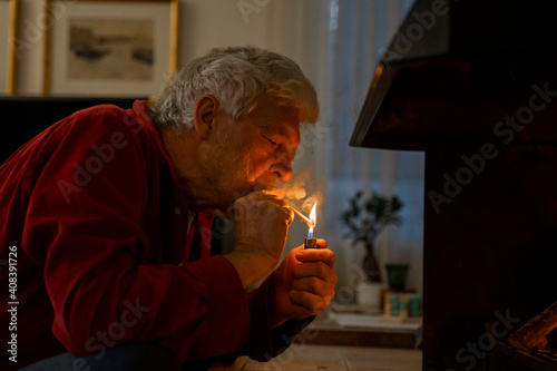 Senior man igniting cigarette with lighter while sitting at home