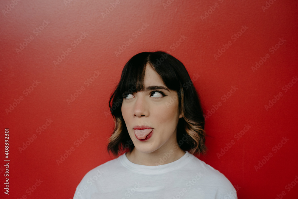 Young woman sticking out tongue while looking up against red background Young woman sticking out tongue while looking up against red background