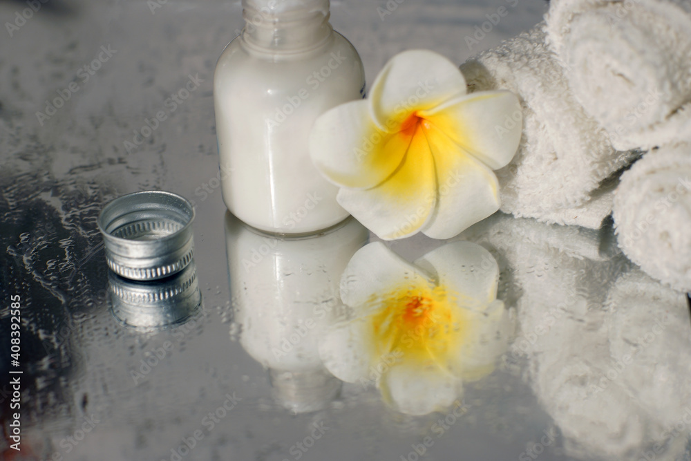 white towel body lotion and plumeria flower are reflected in the mirror surface of the wet table white towel body lotion and plumeria flower are reflected in the mirror surface of the wet table