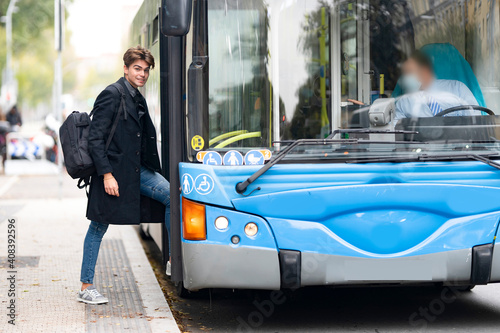 Smiling handsome young man with backpack boarding bus in city photo