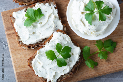 Home made bread on a wooden cutting board with curd cheese and ricotta and herbs. Decorated with green herbs