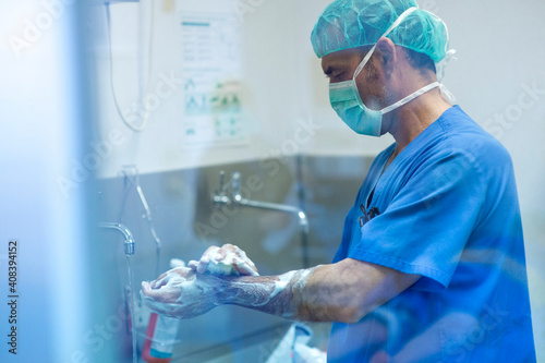 Male orthopedic surgeon washing hand with soap by sink in hospital photo