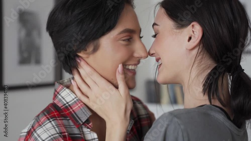 Two happy young affectionate women lesbian lgbtq couple dating lauhging at home together, kissing passionately, hugging enjoying intimate tender sensual moment, bonding in apartment. Lgbt love concept