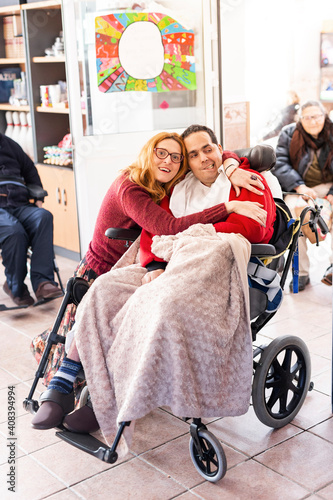 Female caregiver embracing disabled man sitting on wheelchair at nursing home