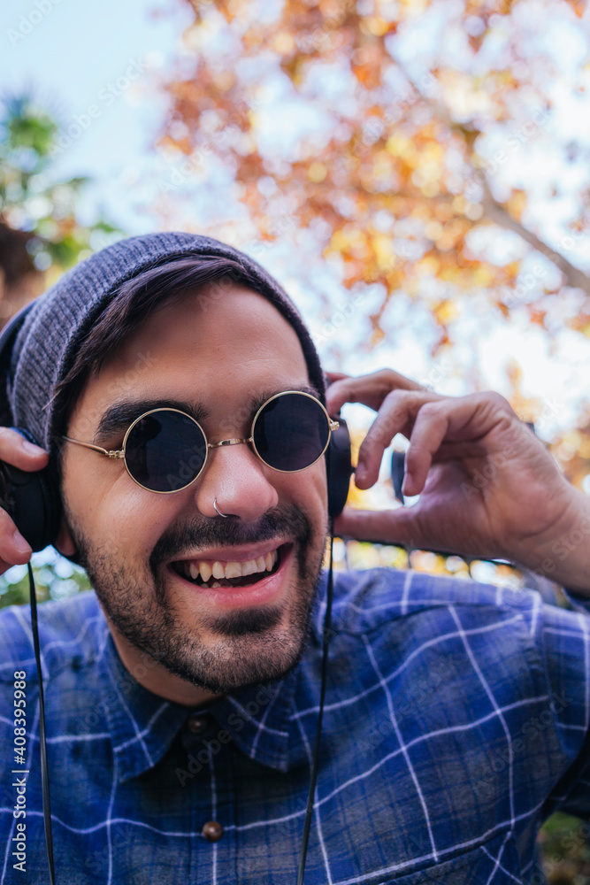 Happy young man in knit hat holding headphones while listening music in public park Happy young man in knit hat holding headphones while listening music in public park