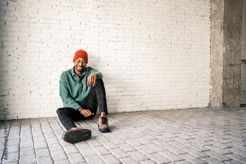 Happy man in knit hat sitting on floor against white brick wall photo