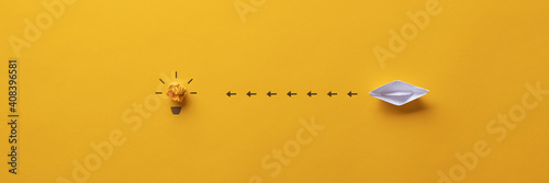 Paper made origami boat sailing towards a light bulb