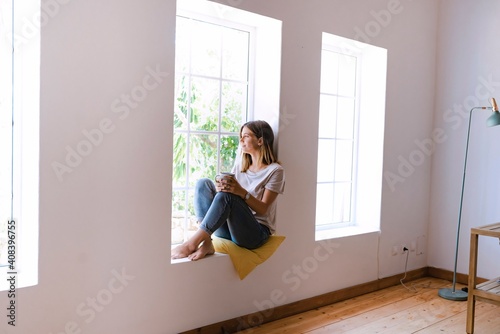 Woman with coffee cup sitting on window sill at home photo