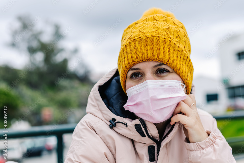 Caucasian woman in close-up with yellow woolen cap, pensive with pink face mask
