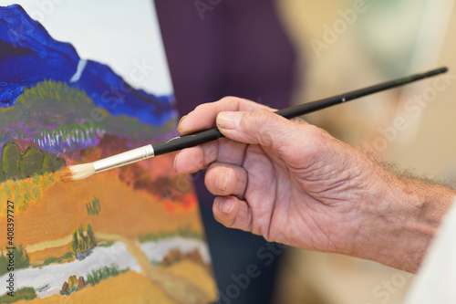 Man's hand holding paintbrush with painting in background