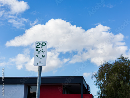 Two hour parking sign with blue sky and white clouds photo