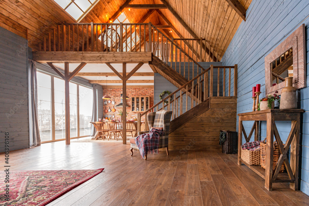 cozy all wooden interior of a country house in a wooden design. spacious living room with kitchen area with large windows. bedroom on the second floor.