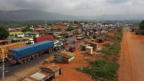 Aerial truck parking in village along highway Ghana Africa 4K. Busy congested market area and truck parking in rural village. Survive in low income poverty of Africa. Vehicles roadside market shops.