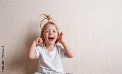 a little beautiful girl sits at home on the floor near the wall and makes funny faces