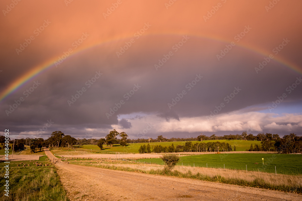 A ground level view looking down a dirt road with a vivid rainbow arching overhead A ground level view looking down a dirt road with a vivid rainbow arching overhead