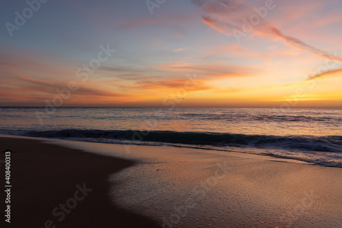 gorgeous colorful sunset over the ocean and beach with gentle waves lapping at the shore