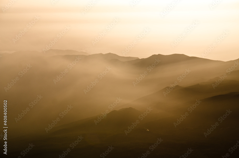 Sun beams passing through dawn mist with silhouettes of mountains, ridges and peaks, Tenerife, Canarian Islands