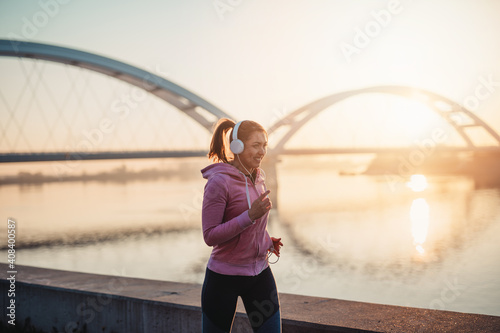 Beautiful young and fit woman in good shape running and jogging alone on city bridge street. She listens to music with headphones. 