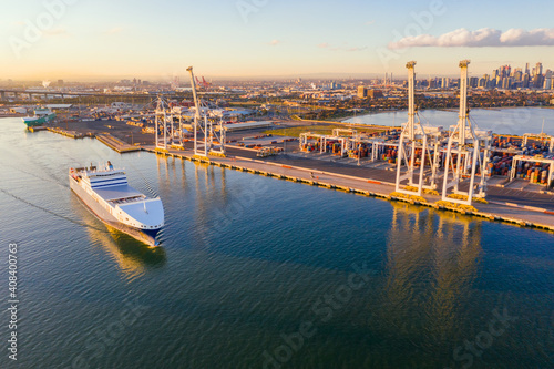 Aerial view of a cargo ship cruising past large gantry cranes on a dock photo