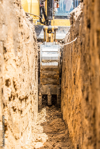 Yellow excavator digging trench with toothed trenching bucket