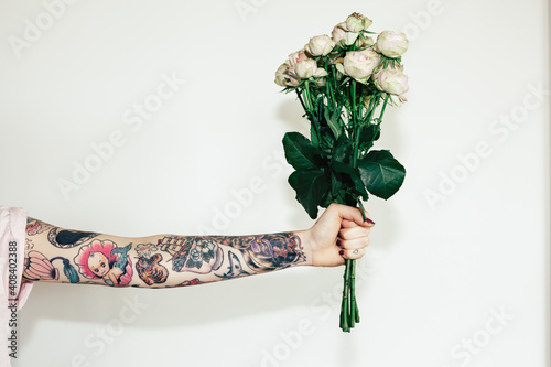 Heavily tattoo'd female arm holding a bunch of thorny pink roses