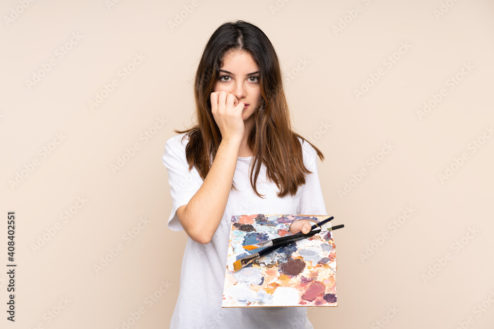 Young artist man holding a palette isolated on beige background nervous and scared Young artist man holding a palette isolated on beige background nervous and scared