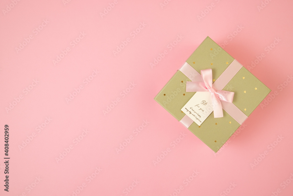 Golden box with ribbon lying on pink background with copy space. Wrapped gift on table with space for text. Valentine s present in flat lay composition.