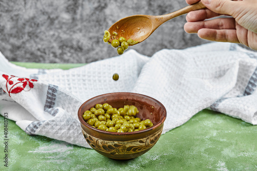 Hand taking a spoon of boiled green peas on a green table photo