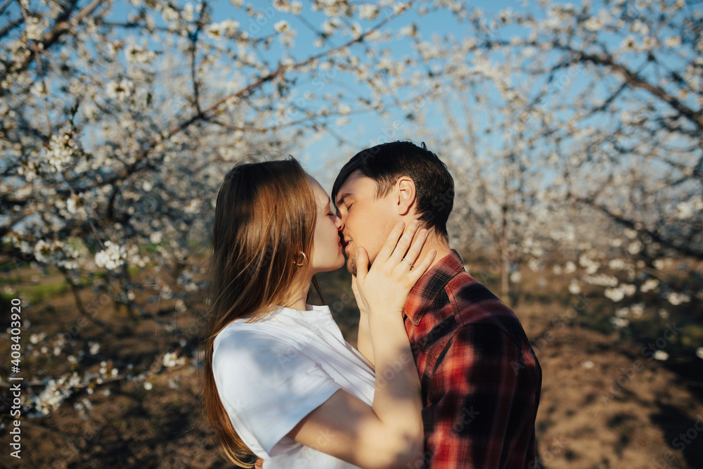 Young passionate couple want to kiss near white spring blossom trees.