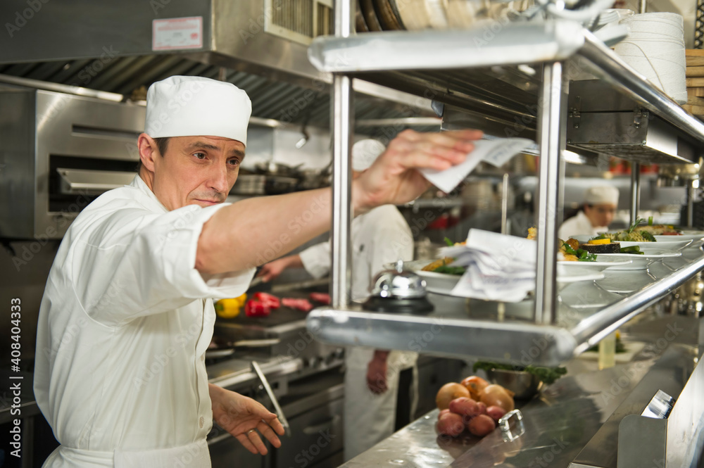 Chef putting order on stick, in background chefs preparing food Chef putting order on stick, in background chefs preparing food