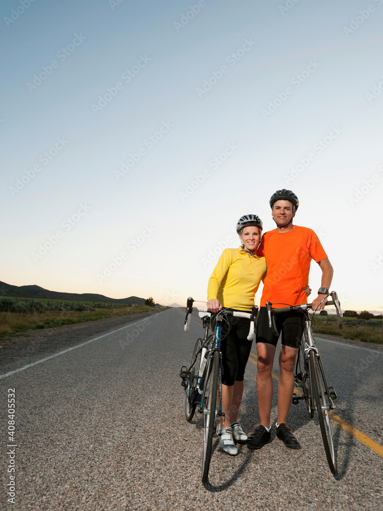 Couple of cyclists posing for portrait on empty road Couple of cyclists posing for portrait on empty road