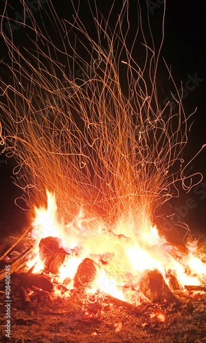 Burning red hot sparks fly from big fire. Beautiful abstract background on the theme of fire. Burning coals, flaming particles flying off against black background.